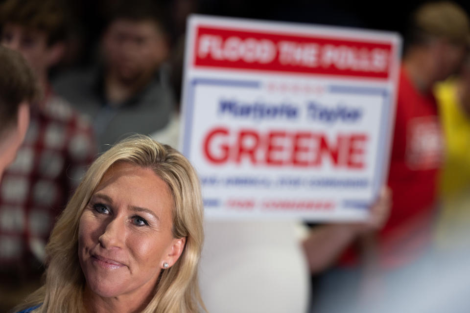 Rep. Marjorie Taylor Greene with a supporter holding a poster behind her that says: Flood the Polls, Marjorie Taylor Greene.