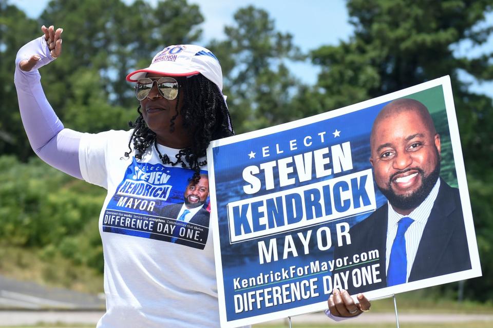 Brenda Miller, of Augusta, waves to passing cars as she helps campaign for mayor candidate Steven Kendrick outside the Julian Smith Casino in Augusta, Ga., on Tuesday, June 21, 2022. 
