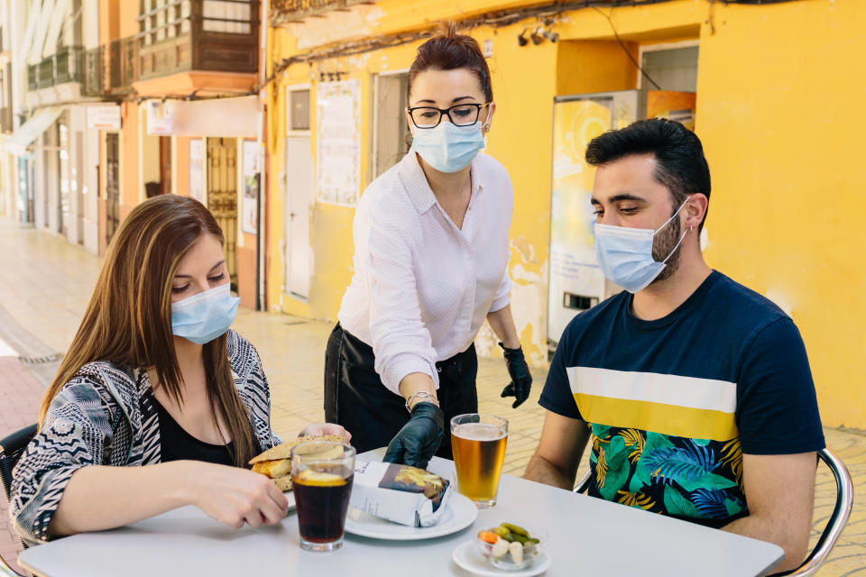 Clients with masks on the terrace of a bar in Spain attended by a waiter with gloves and masks. Social distancing