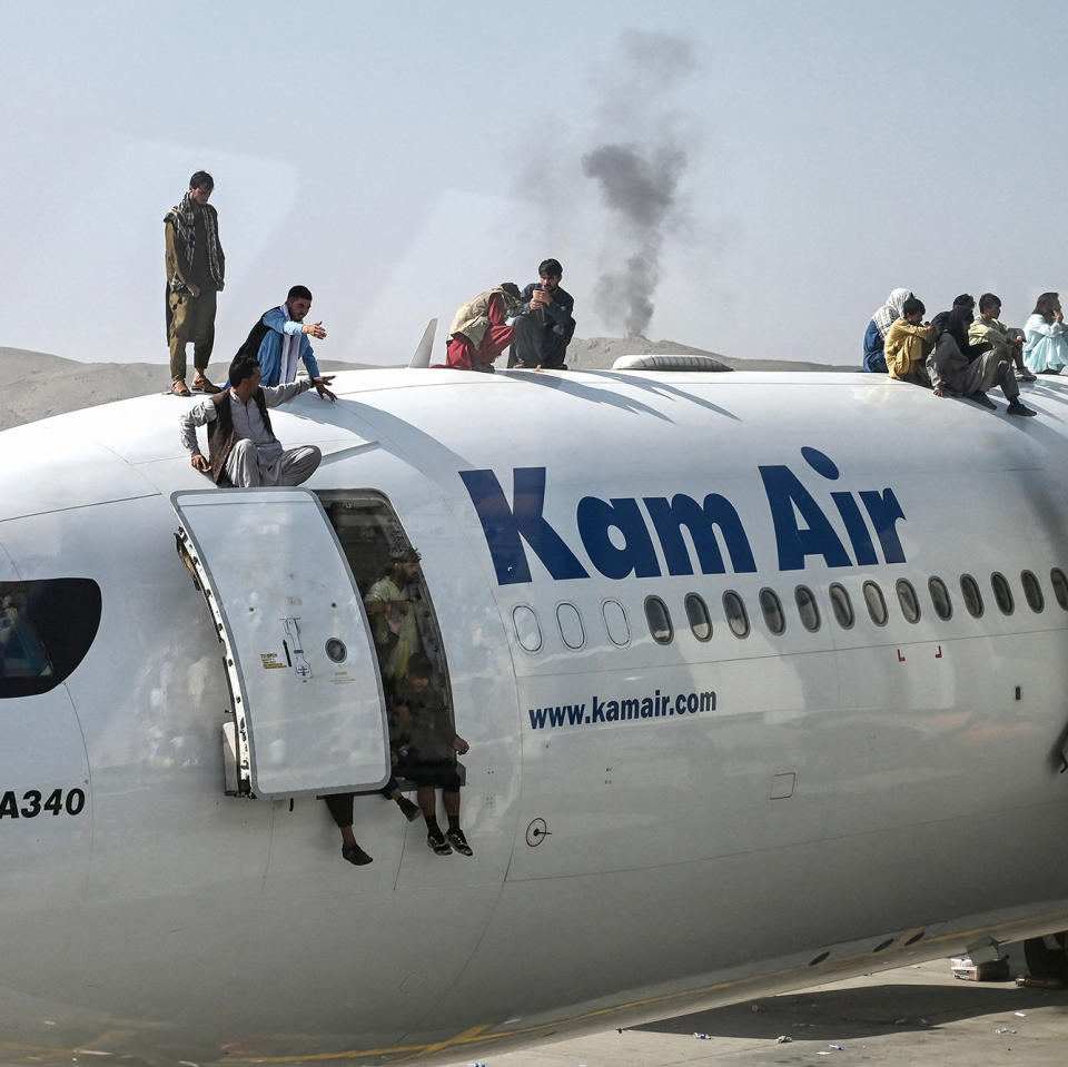 Image: Afghan people climb atop a plane as they wait at the airport in Kabul, Afghanistan. (Wakil Kohsar / AFP via Getty Images)