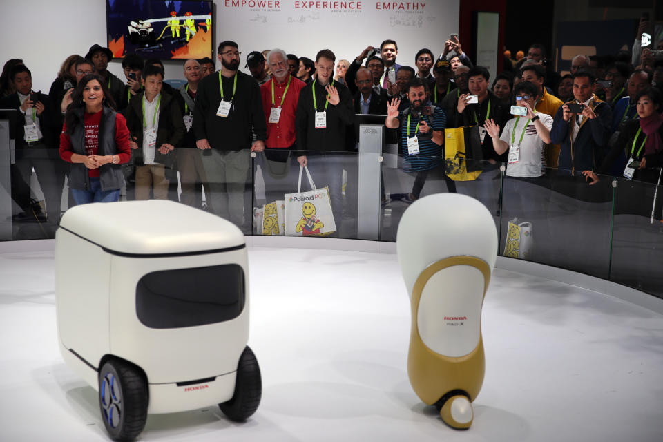 Attendees wave at Honda robotics concepts 3E-C18, left, and 3E-A18 at CES International, Tuesday, Jan. 9, 2018, in Las Vegas. (AP Photo/Jae C. Hong)