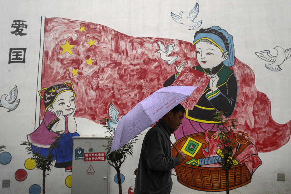 A man holding an umbrella walks by a new village house decorated with a patriotic painting which was built by the Chinese government for ethnic minority members in Ganluo county, southwest China's Sichuan province on Sept. 10, 2020. China's ruling Communist Party says its initiatives have helped to lift millions of people out of poverty. Yi ethnic minority members were moved out of their mountain villages in China’s southwest and into the newly built town in an anti-poverty initiative. (AP Photo/Andy Wong)