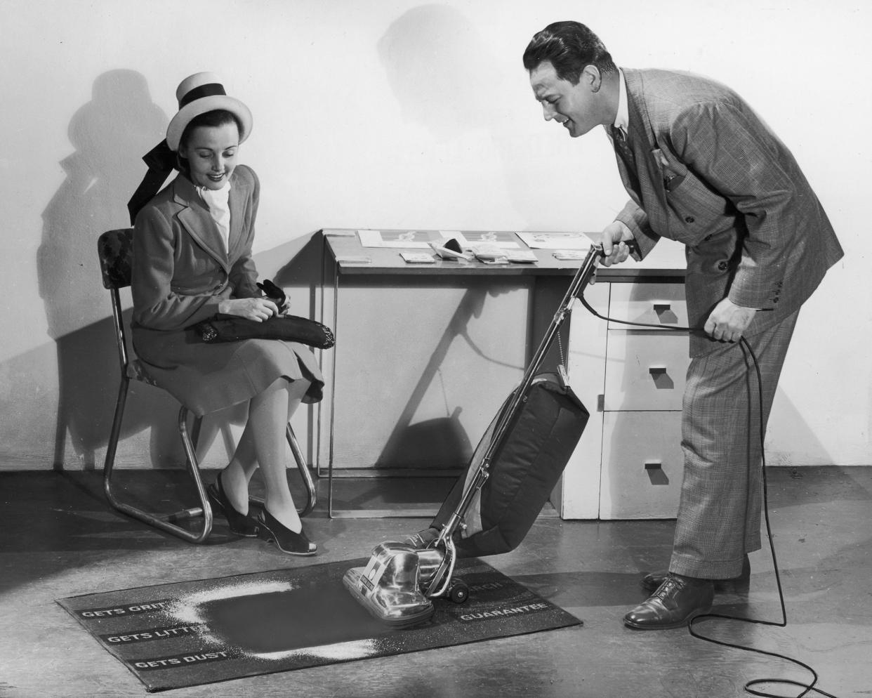 circa 1955: A salesman demonstrates the effectiveness of a General Electric vacuum cleaner to a prospective customer.