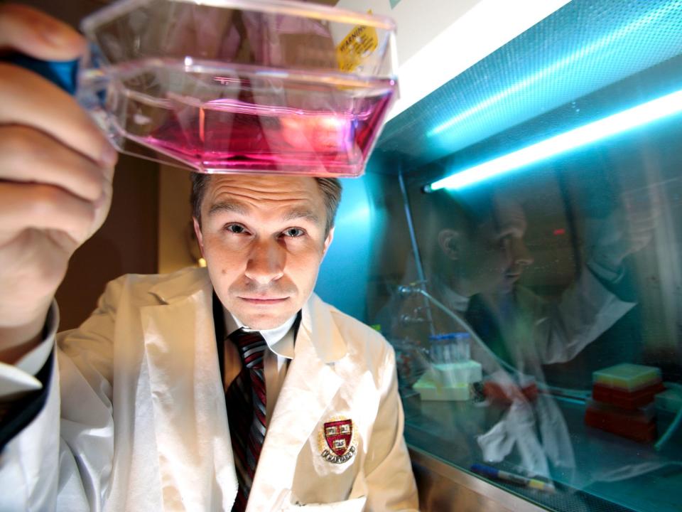 David Sinclair wearing a lab coat while he inspects a clear flask of pink liquid in his lab.