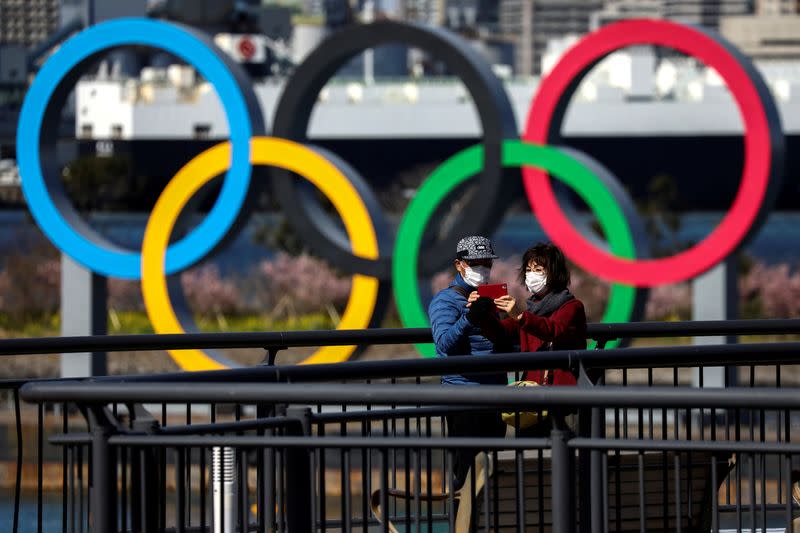 FILE PHOTO: People wearing protective face masks are seen in front of the Giant Olympic rings at the waterfront area at Odaiba Marine Park in Tokyo