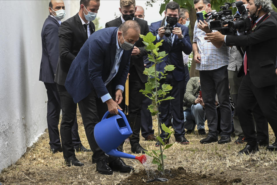 Turkish Foreign Minister Mevlut Cavusoglu, waters a newly planted plane tree at a muslim cemetery at Komotini town, in northeastern Greece, Sunday, May 30, 2021. Greece's prime minister said Friday his country is seeking improved ties with neighbor and longtime foe Turkey, but that the onus is on Turkey to refrain from what he called "provocations, illegal actions and aggressive rhetoric." (AP Photo/Giannis Papanikos)