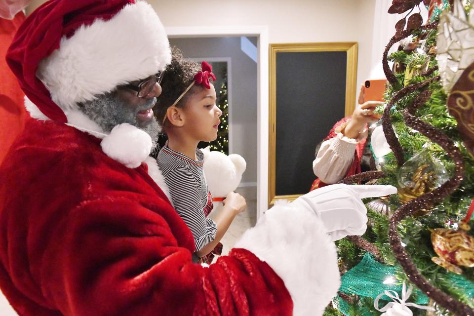 Shawn Coley (Santa) inspects the ornaments on the Christmas tree with Laila Williams during a Selfies with Santa photo session Wednesday evening, December 15, 2021. Natasha Spencer-Coley and her husband Shawn Coley offer their services at events as Mr and Mrs Santa Claus during the holiday season but also have their Ft. Caroline Road home set up for private photo session with Santa. For a fee, families can bring their children for a 45 minute session with a variety of Christmas settings to take their own photos or have them taken by Mrs Claus in a relaxed setting which allows the most hesitant children to put down their guard. [Bob Self/Florida Times-Union]