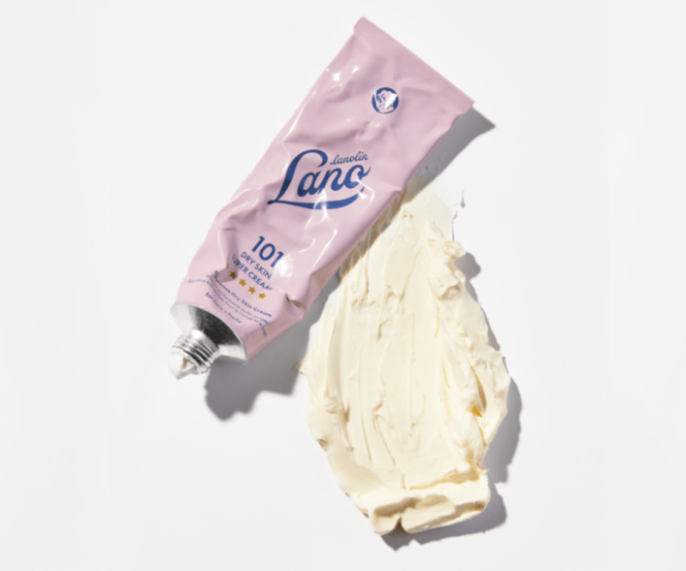 A crumpled pink tube of Lanolips' 101 Dry Skin Super Cream lies on a pale grey background with a mass of the cream product smeared on its right.