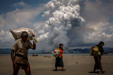 FILE PHOTO: Smoke is seen on the Myanmar border as Rohingya refugees walk on the shore after crossing the Bangladesh-Myanmar border by boat through the Bay of Bengal, in Shah Porir Dwip, Bangladesh September 11, 2017. REUTERS/Danish Siddiqui/File Photo