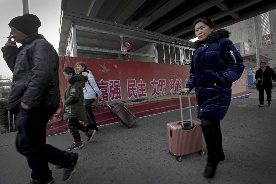 In this Jan. 12, 2019, photo, Chinese people walk by a worker welding steel frames near a billboard displaying a Chinese government propaganda message at the Central Business District in Beijing. China's slowing economy is squeezing the urban workers and entrepreneurs the ruling Communist Party is counting on to help transform this country from a low-wage factory floor into a prosperous consumer market. (AP Photo/Andy Wong)