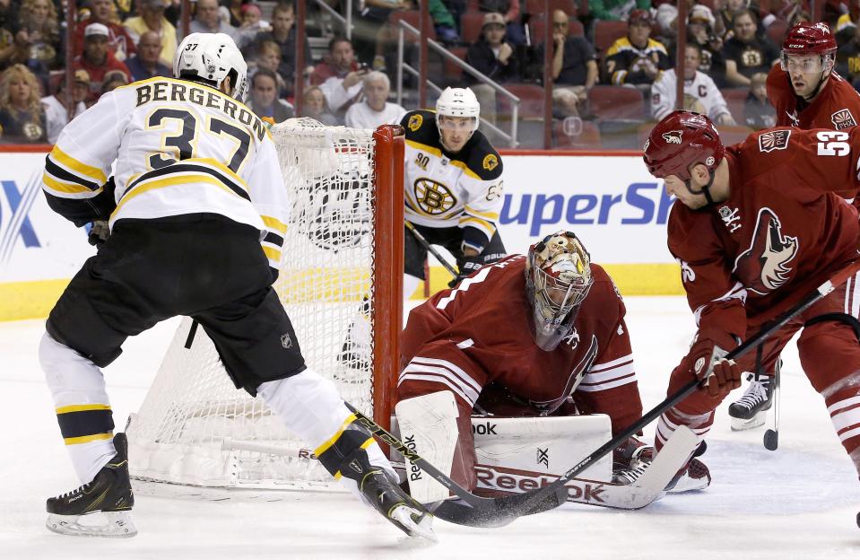 Boston Bruins' Patrice Bergeron (37) scores a goal against Phoenix Coyotes' Mike Smith, third from the left, as Coyotes' Derek Morris (53) defends and Coyotes' Keith Yandle, back right, and Bruins' Brad Marchand (63) look on during the first period of an NHL hockey game on Saturday, March 22, 2014, in Glendale, Ariz. (AP Photo/Ross D. Franklin)