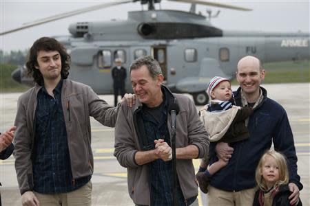 Didier Francois (C), former French hostage and journalist, reacts as he stands between Edouard Elias (L) and Nicolas Henin (R), who holds his children, moments after their arrival by helicopter from Evreux to the military airbase in Villacoulbay, near Paris, April 20, 2014. REUTERS/Gonzalo Fuentes