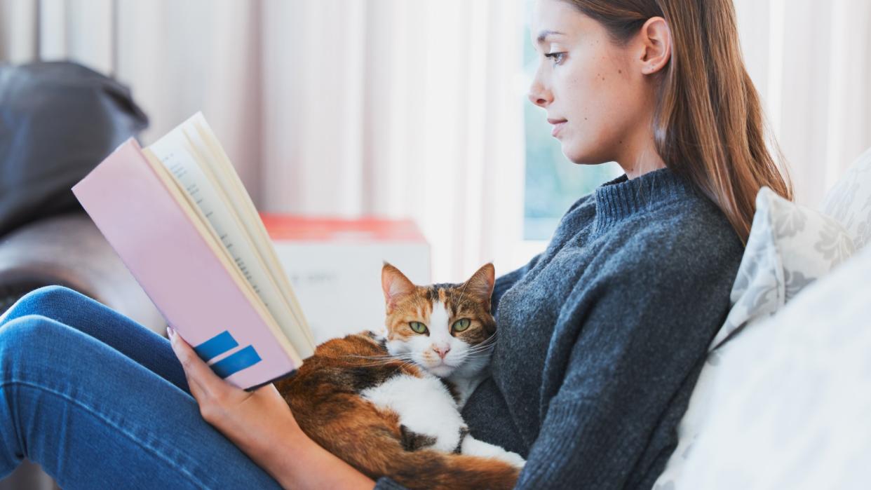  Woman reading book with cat on her lap. 