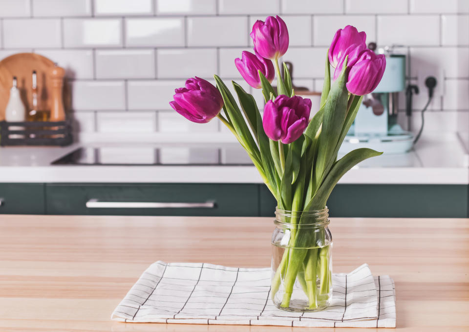 Purple tulips in a glass jar standing on the modern kitchen with white tile