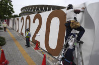 FILE - In this June 2, 2021, file photo, workers paste the overlay on the wall of the National Stadium, in Tokyo. The Tokyo Olympics are not looking like much fun: Not for athletes. Not for fans. And not for the Japanese public, who are caught between concerns about the coronavirus at a time when few are vaccinated on one side and politicians and the International Olympic Committee who are pressing ahead on the other. (AP Photo/Eugene Hoshiko, File)