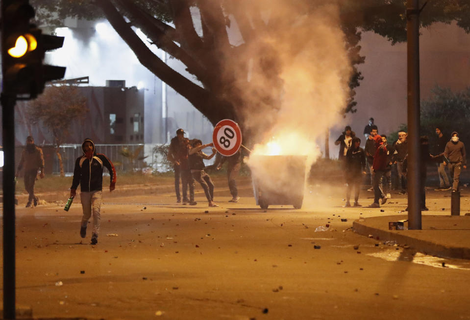 Anti-government protesters burn garbage container and throw glass bottles towards riot police during a protest in downtown Beirut, Lebanon, Saturday, Dec. 14, 2019. The recent clashes marked some of the worst in the capital since demonstrations began two months ago. The rise in tensions comes as politicians have failed to agree on forming a new government. (AP Photo/Hussein Malla)