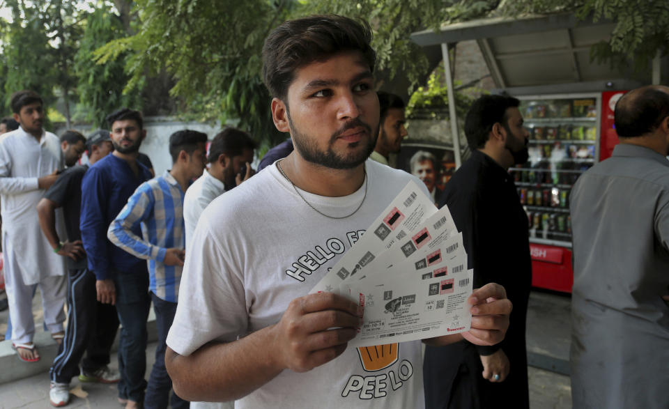 A fan displays tickets of an upcoming cricket match between Pakistan and Sri Lanka while others waiting for their turn outside a bank in Lahore, Pakistan, Saturday, Sept. 21, 2019. Pakistan recalled all-rounders Iftikhar Ahmed and Mohammad Nawaz for three-match one-day international series against Sri Lanka, starting at Karachi from next week. (AP Photo/K.M. Chaudary)