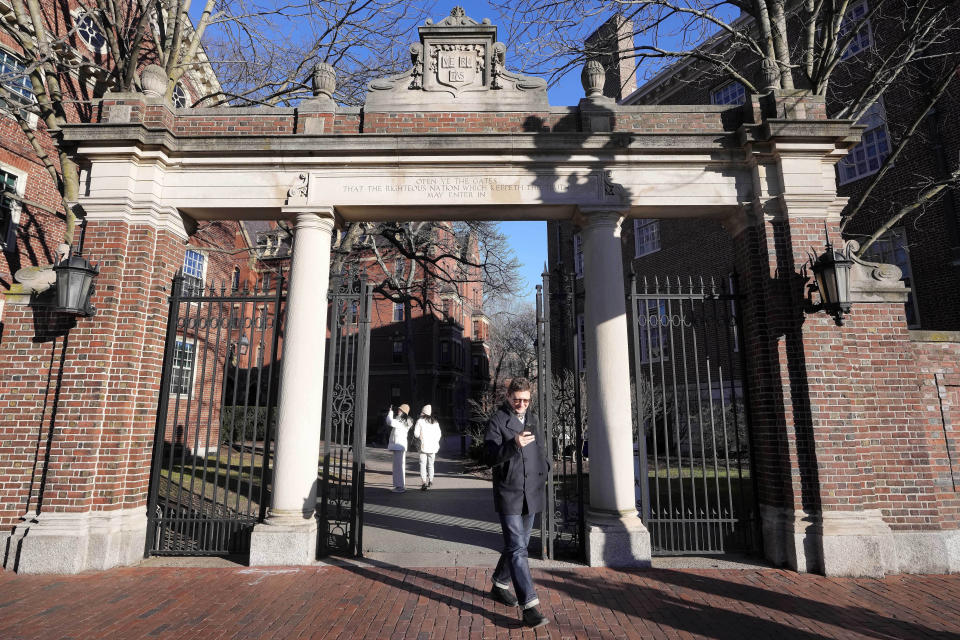 CORRECTS DOLLAR AMOUNT FROM $90,000 TO $95,000 - FILE - A passer-by walks through a gate to the Harvard University campus, Jan. 2, 2024, in Cambridge, Mass. As more than 2 million graduating high school students from across the United States finalize their decisions on what college to attend this fall, many are facing jaw-dropping costs — in some cases, as much as $95,000. (AP Photo/Steven Senne, File)