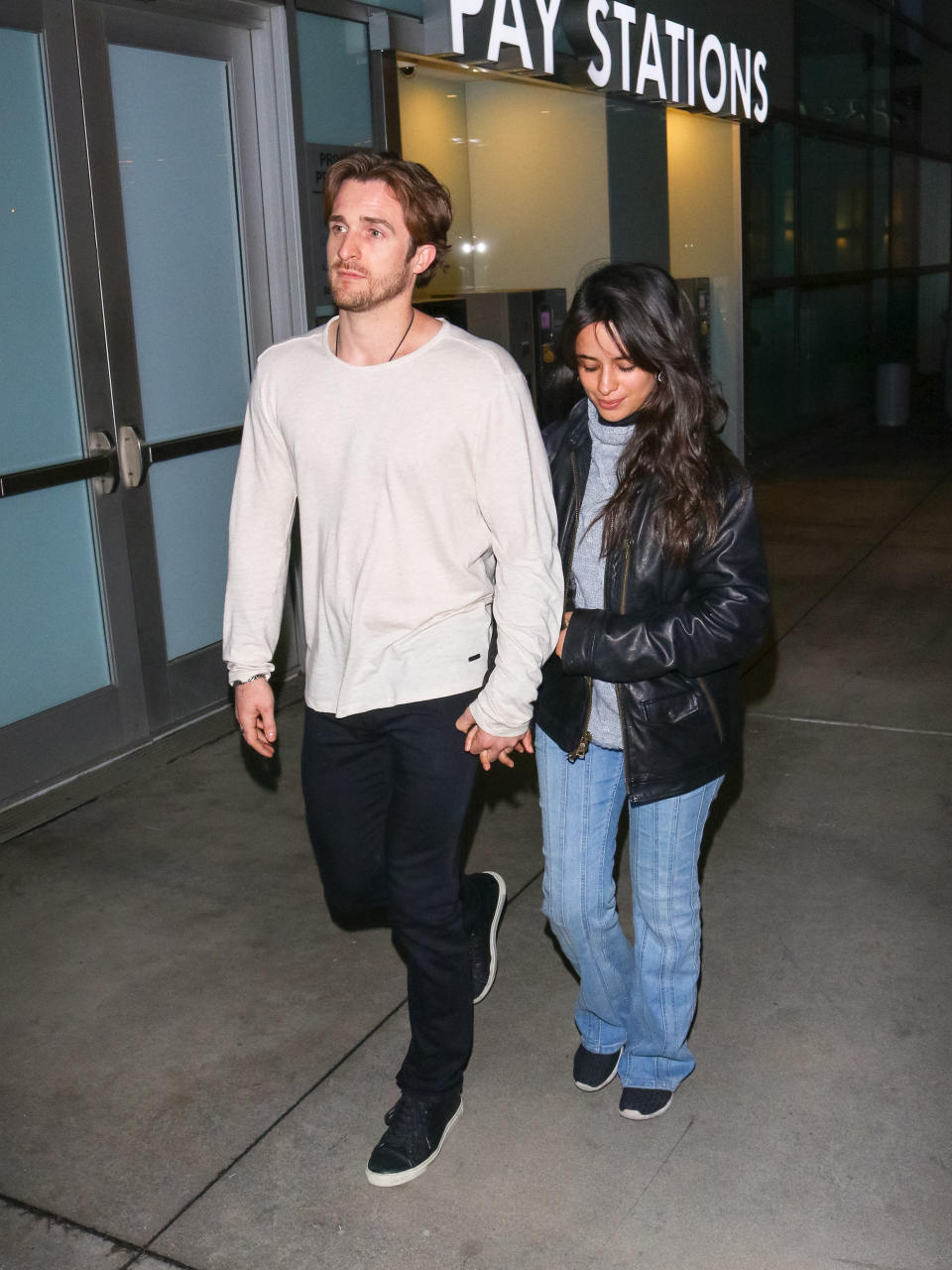 Matthew Hussey and Camilla Cabello holding hands while walking outside a building at night