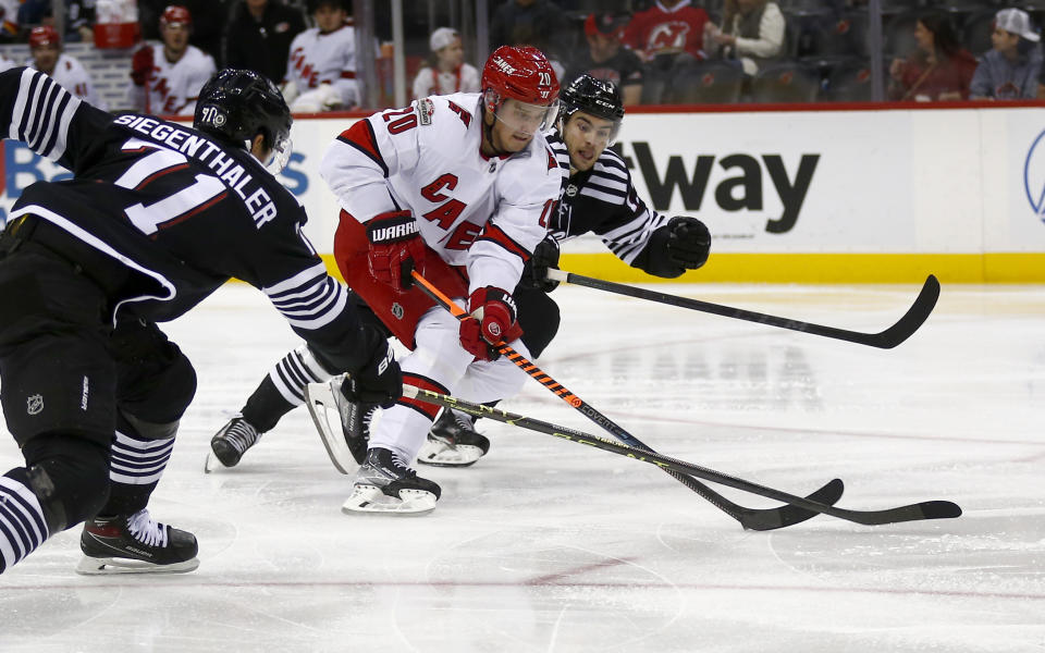 Carolina Hurricanes center Sebastian Aho (20) skates between New Jersey Devils defenseman Jonas Siegenthaler, left, and center Nico Hischier during the second period of an NHL hockey game, Sunday, Jan. 1, 2023, in Newark, N.J. (AP Photo/John Munson)