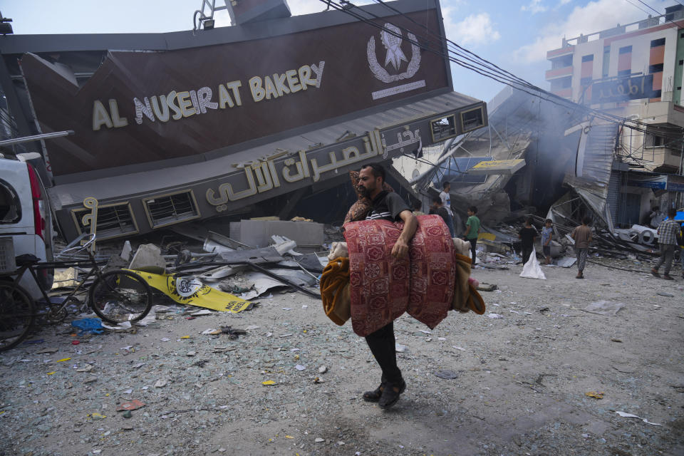 Palestinians walk by the destroyed building of Al Nuseirat Bakery in an Israeli airstrike Nusseirat refugee camp Gaza Strip, Wednesday, Oct. 18, 2023. (AP Photo/Hatem Moussa)