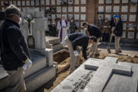 A priest and relatives pray as a victim of the COVID-19 is buried by undertakers at the Almudena cemetery in Madrid, Spain, Saturday March 28, 2020. In Spain, where stay-at-home restrictions have been in place for nearly two weeks, the official number of deaths is increasing daily. The new coronavirus causes mild or moderate symptoms for most people, but for some, especially older adults and people with existing health problems, it can cause more severe illness or death. (AP Photo/Olmo Calvo)