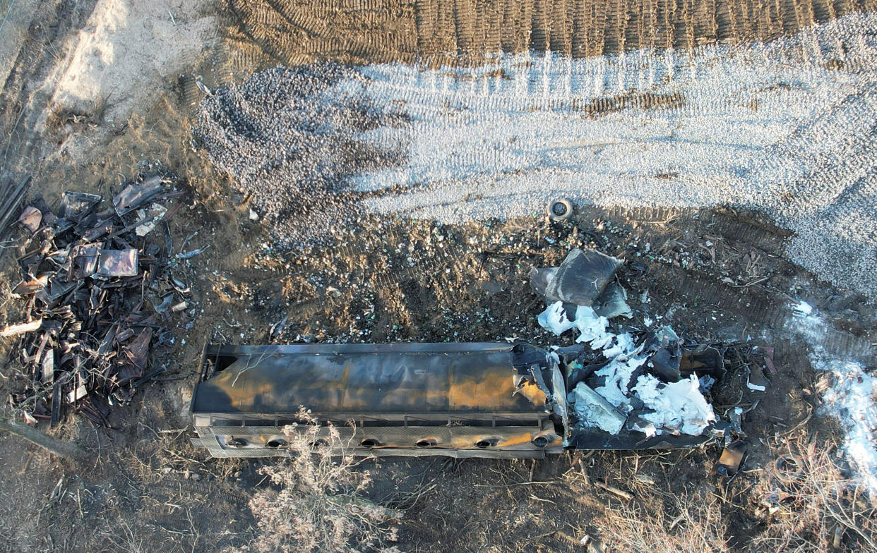 A burnt container with white charred metal surrounded by debris and gravel at the site.