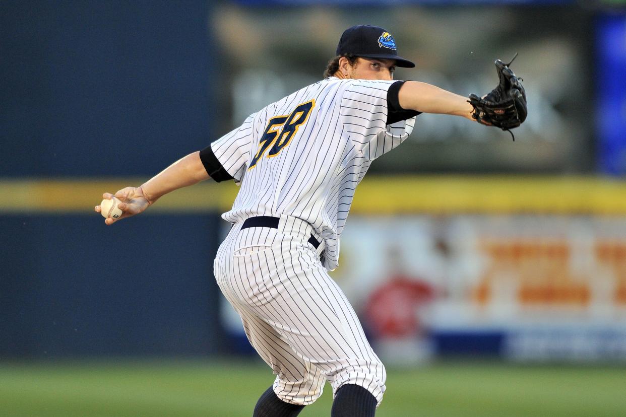 Focus on Nik Turley Delivering a pitch while on the mound in a baseball game with a blurred background of the baseball field and bleachers