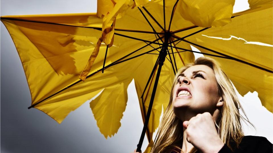Una mujer enojada con un paraguas amarillo roto bajo la lluvia.