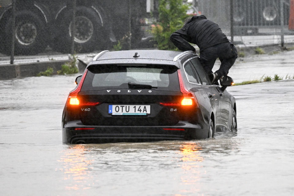A man climbs out of a car which got stuck at a flooded roundabout in Arlöv, along the E6 road outside Malmö, southern Sweden, Monday, Aug. 7, 2023. Stormy weather across the Baltic Sea region is causing airport delays, suspended ferry service, minor power outages and lots of rain. (Johan Nilsson/TT News Agency via AP)