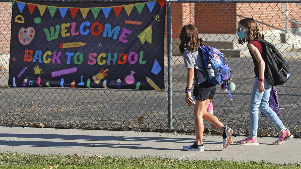 FILE - In this Aug. 17, 2020, file photo, Cimmie Hunter, left, and Cadence Ludlow, both 6th graders, arrive at Liberty Elementary School during the first day of class in Murray, Utah. For countless families across the country, the school year is opening in disarray and confusion, with coronavirus outbreaks triggering sudden closings, mass quarantines and deep anxiety among parents. (AP Photo/Rick Bowmer, File)