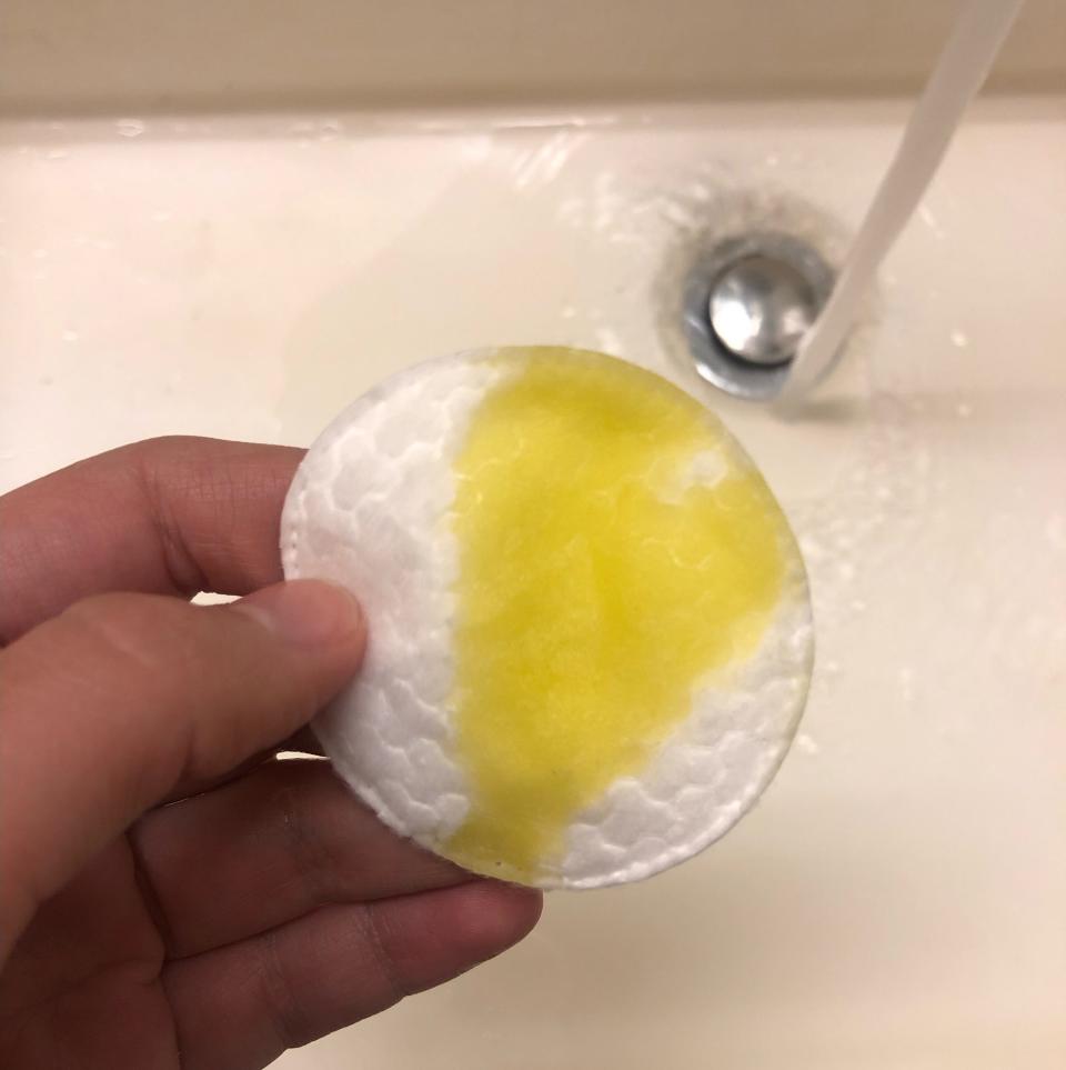 A hand holding a cotton pad with olive oil on it.