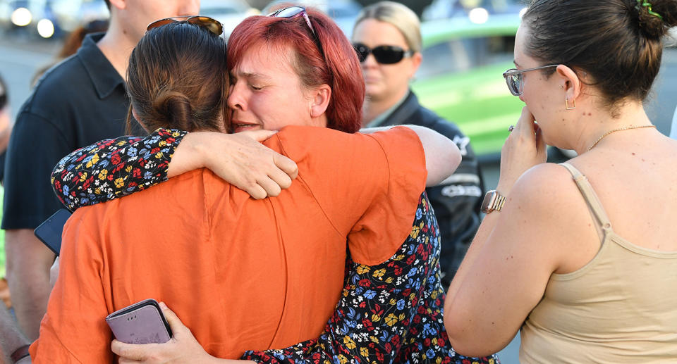 People are seen consoling each other at a vigil for Kate Leadbetter, 31, and Matthew Field, 37, who were killed while walking their dogs on Australia Day, Brisbane, Wednesday, January 27, 2021. A teenager has been charged with murder after the allegedly stolen Landcruiser he was driving struck and killed the couple in Brisbane. (AAP Image/Darren England) NO ARCHIVING