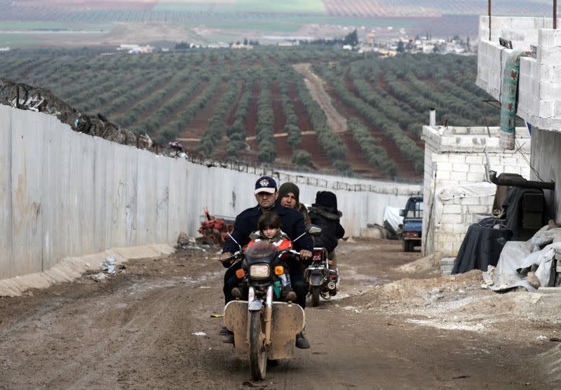 An Internally displaced Syrian man rides a motorbike near the wall in Atmah IDP camp, located near the border with Turkey