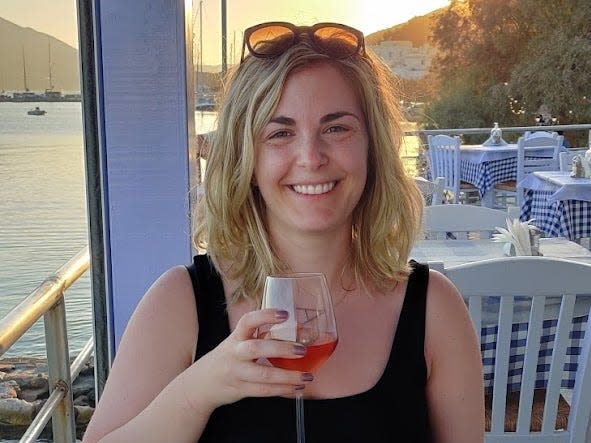 the writer holding a glass of wine at dinner with the sun setting in the background