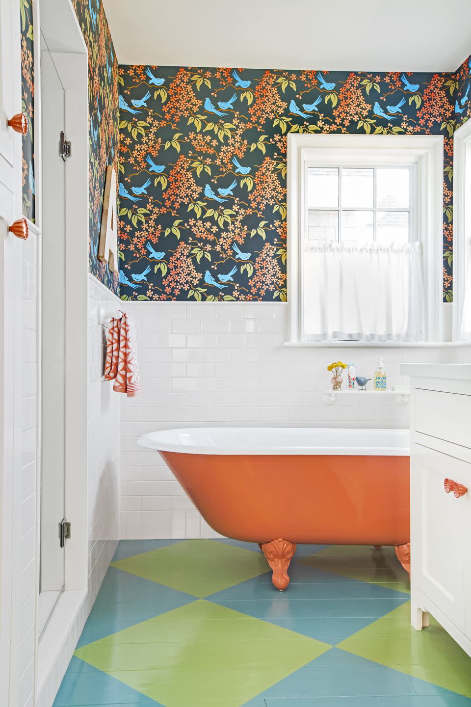 colorful bathroom with blue and green painted floor, orange painted clawfoot tub, and patterned wallpaper