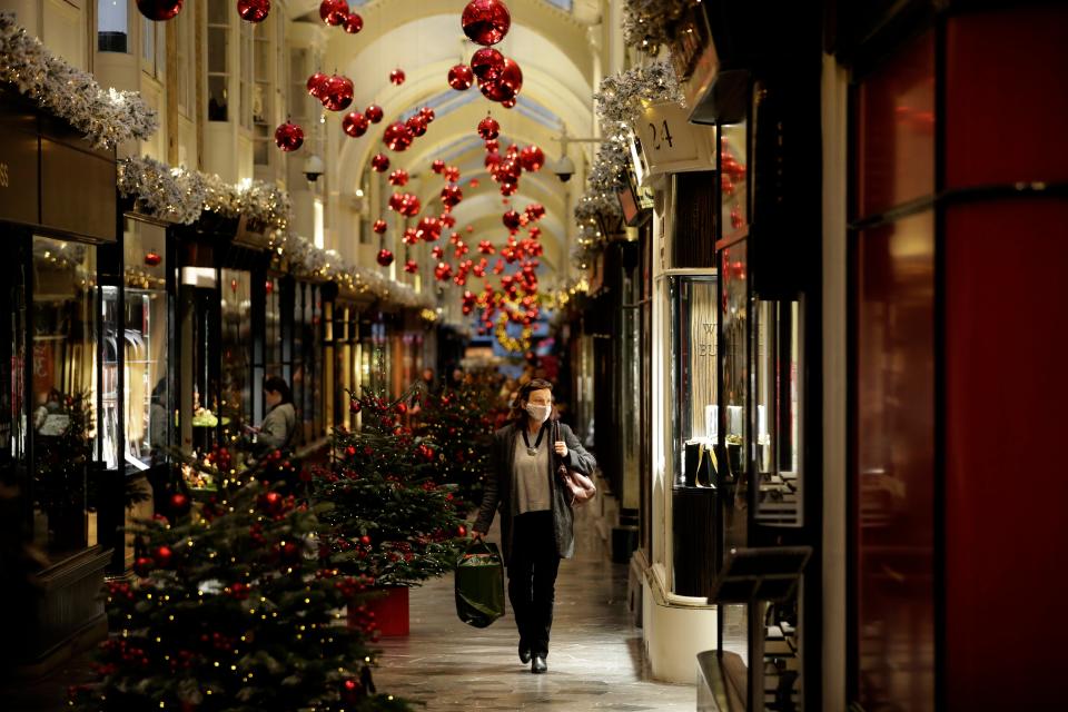 <p>A woman wearing a face mask walks past Christmas trees and decorations in Burlington Arcade, London</p>AP