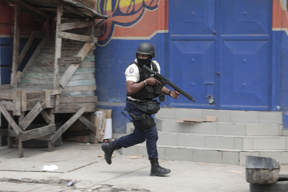 A police officer takes cover during an anti-gang operation in the Portail neighborhood of Port-au-Prince, Haiti, Tuesday, April 25, 2023, a day after a mob in the Haitian capital pulled 13 suspected gang members from police custody at a traffic stop and beat and burned them to death with gasoline-soaked tires. (AP Photo/Odelyn Joseph)