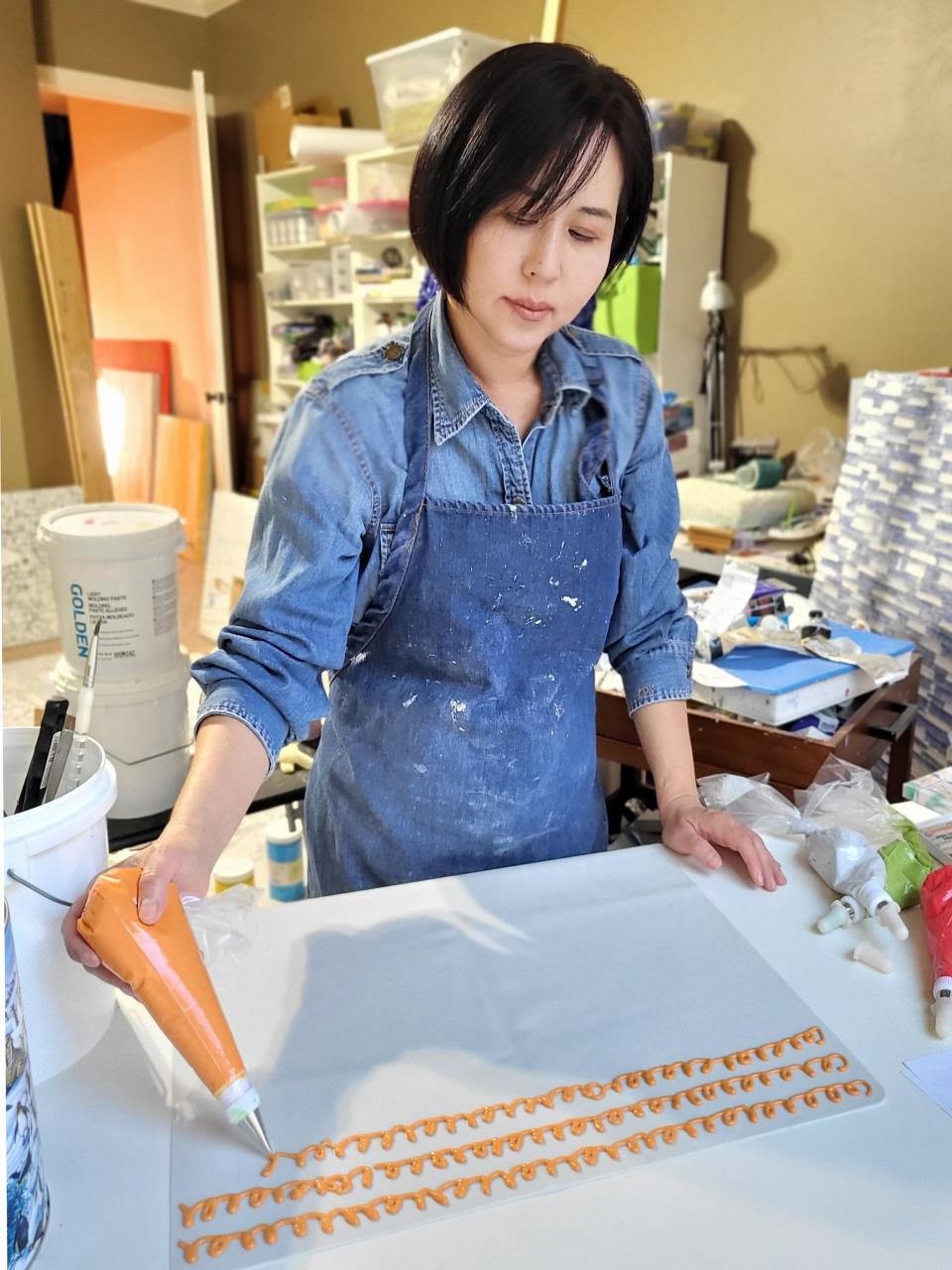 Karam, a Korean American artist based in Edmond, works in her studio. Over the past eight years, she has become known for creating what she calls "unpainted paintings," using a pastry bag rather than a paintbrush to apply a paint mixture to her canvases.