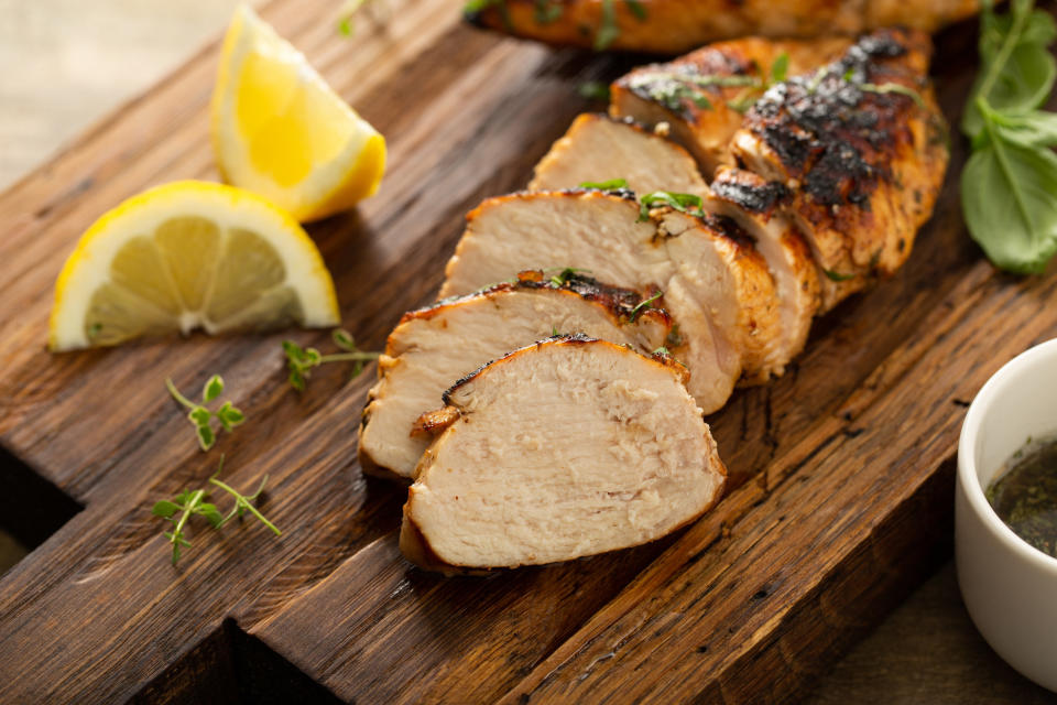 Balsamic grilled chicken breast with fresh herbs sliced on a rustic wooden board.