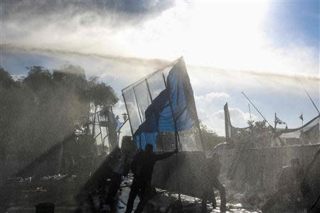 Riot policemen use water canon as anti-government protesters take cover behind a barricade during clashes with police near the Government House in Bangkok December 1, 2013. REUTERS/Athit Perawongmetha