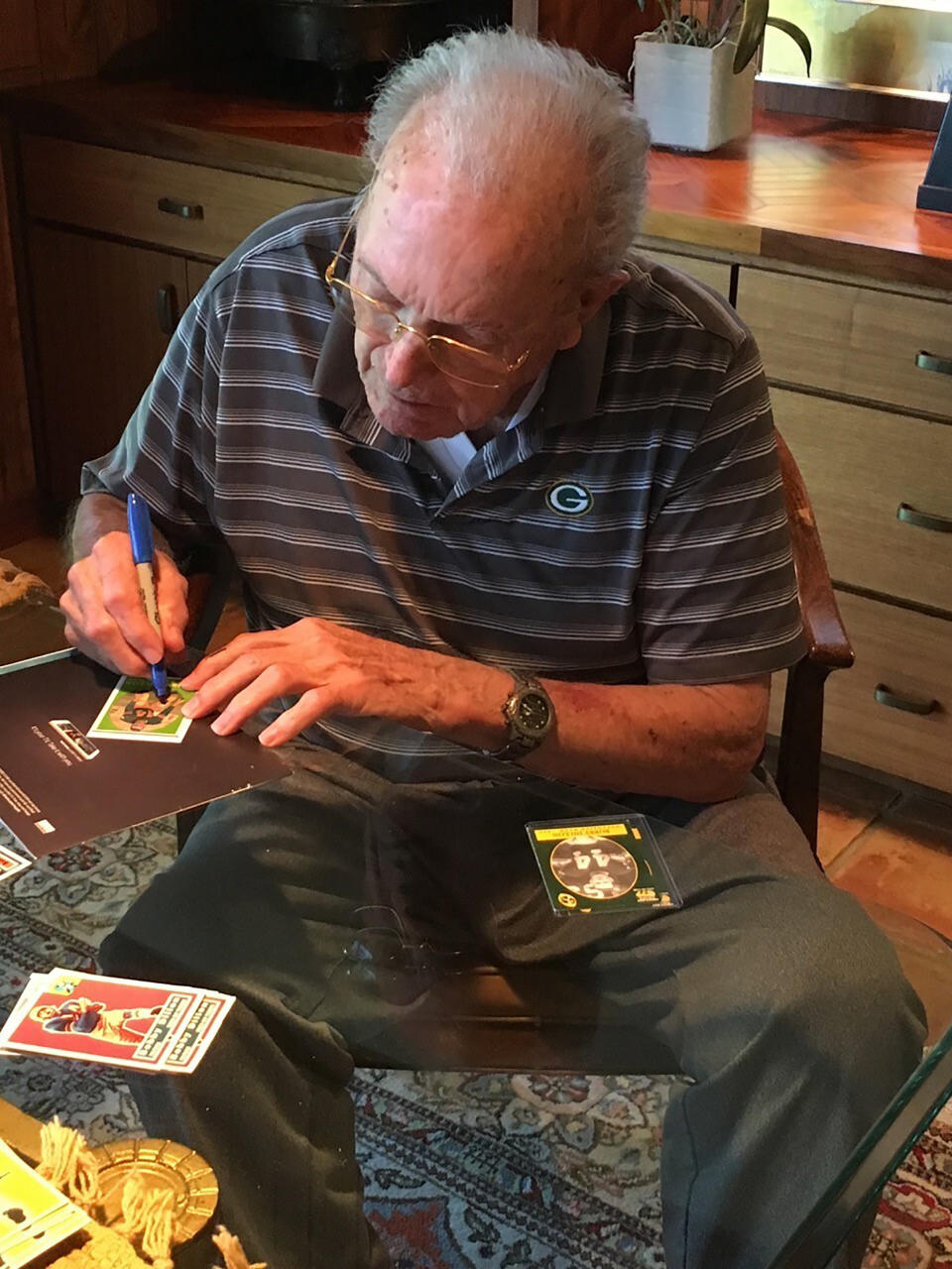 In this June 2019 photo provided by Karen Gooch, former Green Bay Packers football player Bobby Dillon autographs football cards at his home in Temple, Texas. Dillon was one of the best defensive players in the league. But the Packers were an NFL weakling at the time, going 33-61-2 while Dillon was playing safety so well he made four All-Pro teams and intercepted 52 passes. Dillon passed away at age 89 in August 2019, five months before he was selected for the Hall of Fame as part of the centennial class. (Karen Gooch via AP)
