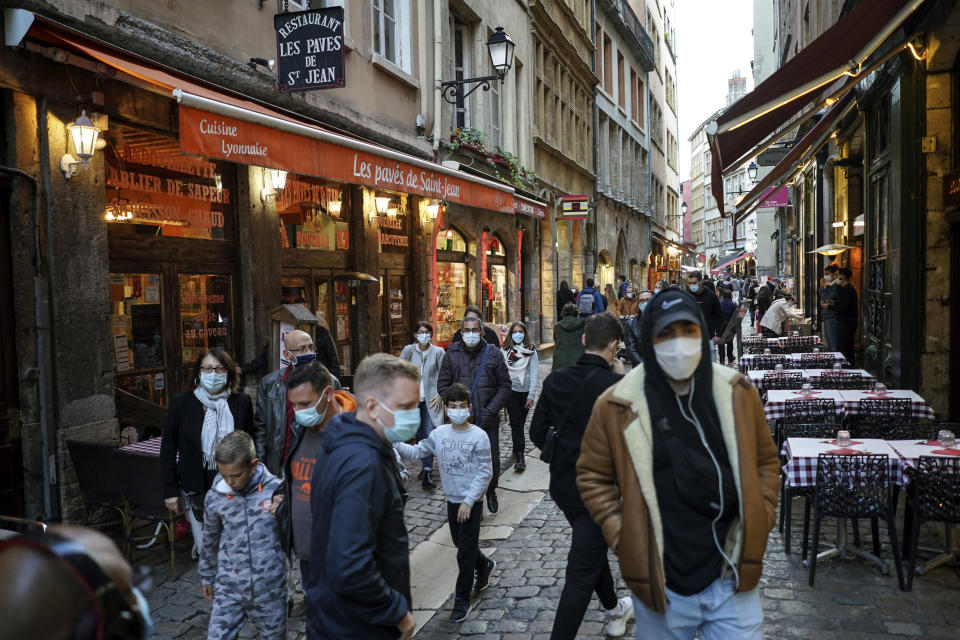 People wearing masks pass by restaurants in the center of Lyon, central France, Saturday, Oct. 10, 2020. Starting Saturday, Lyon has been placed under maximum virus alert. The maximum alert level implies shutting down bars, implementing stricter measures in restaurants and limiting private gatherings. (AP Photo/Laurent Cipriani)