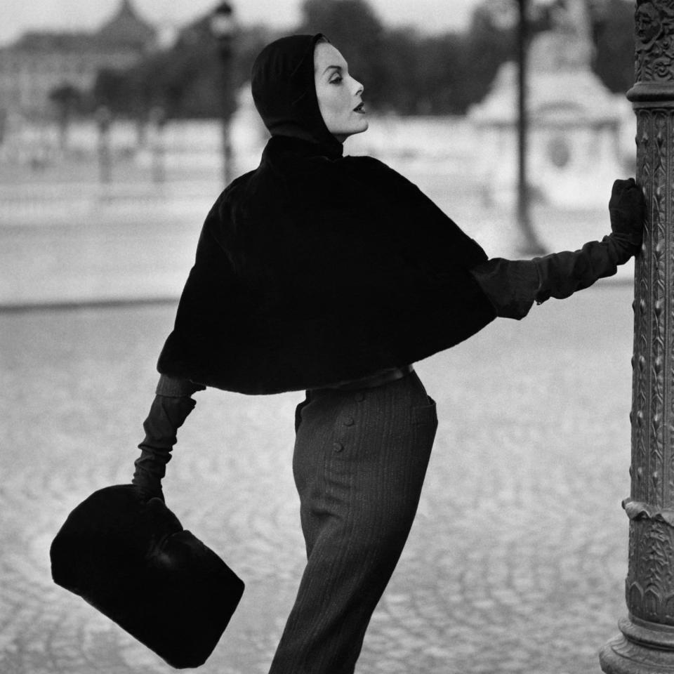 “Paris Furring, Sealskin slip-cover cape: Balmain. The new movement at the shoulders of Balmain’s darkly striped tweed dress—a close-shaped cape of black Alaska sealskin, that slips over the head and closes invisibly via a hidden zipper. The head it’s slipped over here, wearing one of Paulette’s new “cagoulard” caps, a black jersey hood cut long enough to form a gilet.”