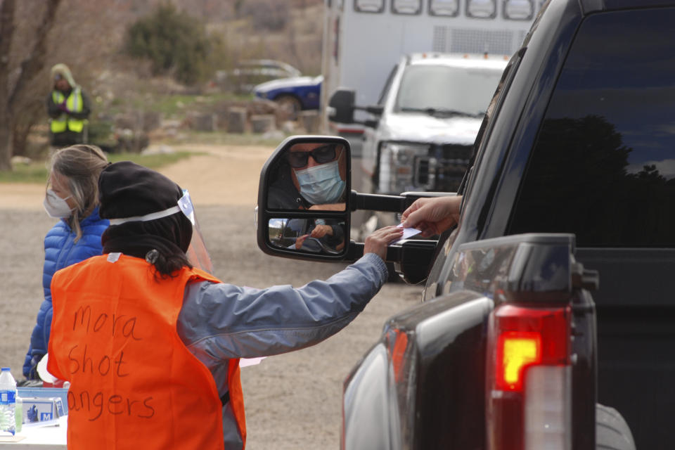 A medical worker hands an updated vaccination card to a motorist at a drive-thru immunization clinic at a motor inn in Mora, N.M., on Tuesday, April 20, 2021. New Mexico is among the states with the highest rates of vaccination for COVID-19. Vaccine crews also traveled down dirt roads to visit homebound elderly residents in sprawling Mora County, with just 4,500 residents who are 80% Latino. First Lady Jill Biden kicked off of a visit to the U.S. Southwest with a tour of a vaccination clinic in Albuquerque. (AP Photo/Morgan Lee)