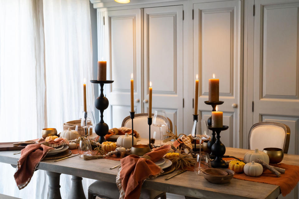 halloween table decor with black candlesticks, rust candles, rust napkins, pumpkins, wooden bowls, tableware