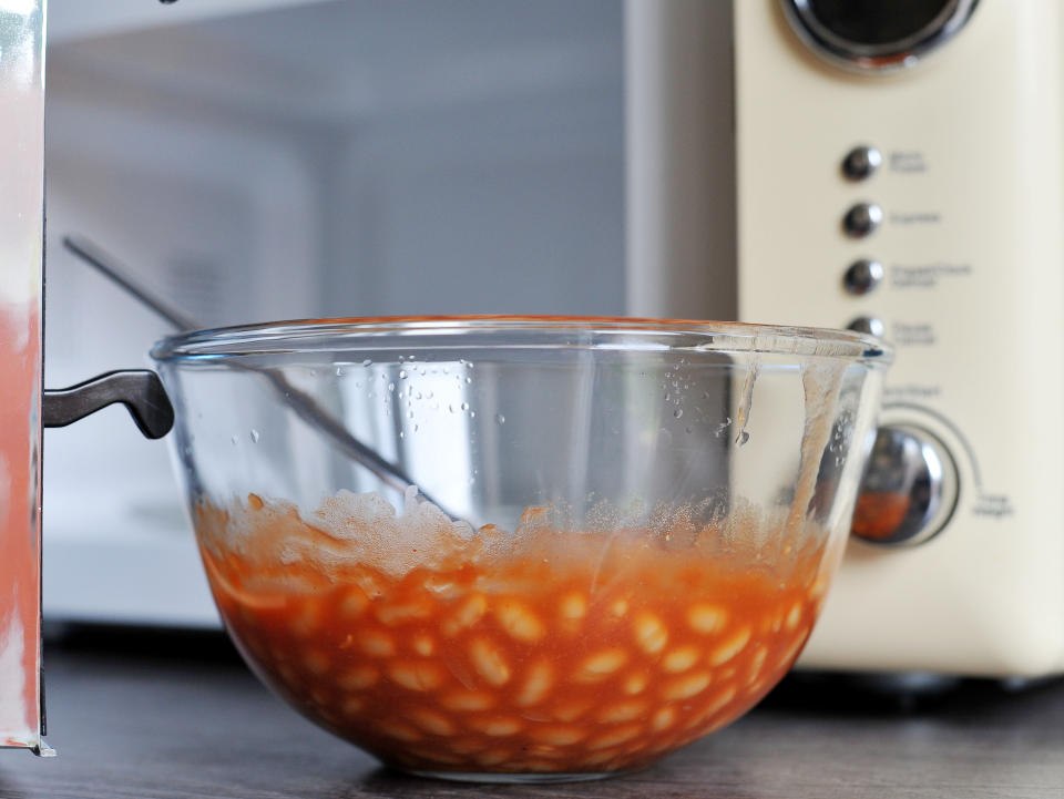 A bowl of baked beans next to a microwave cooker.