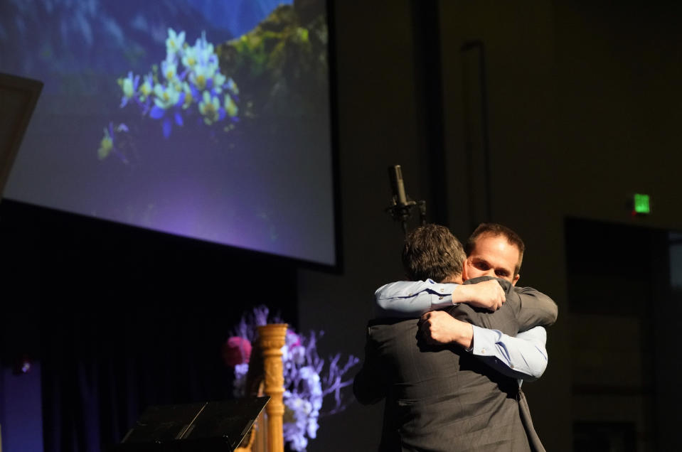 Tom Tonelli, facing camera, a teacher at Columbine High School, hugs former principal Frank DeAngelis during a faith-based memorial service for the victims of the school nearly 20 years earlier, at a community church, Thursday, April 18, 2019, in Littleton, Colo. (Rick Wilking/Pool Photo via AP)