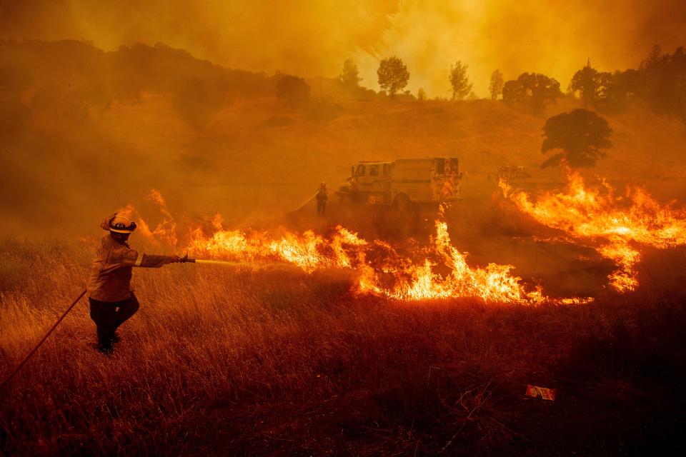 July 1, 2018: A firefighter scrambles to stop a wildfire as wind drives embers across Highway 20 near Clearlake Oaks, Calif.