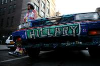 La artista Gretchen Baer luce un traje customizado con imágenes de Hillary Clinton junto a su coche pintado en su apoyo durante un acto de campaña, el 17 de abril de 2016, en la ciudad de Nueva York. (GETTY IMAGES NORTH AMERICA/AFP | JUSTIN SULLIVAN).